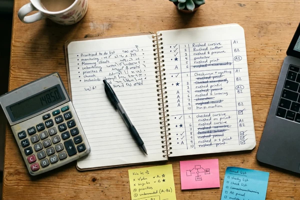 Open planning notebook with a calculator, sticky notes and a laptop on a wooden desk
