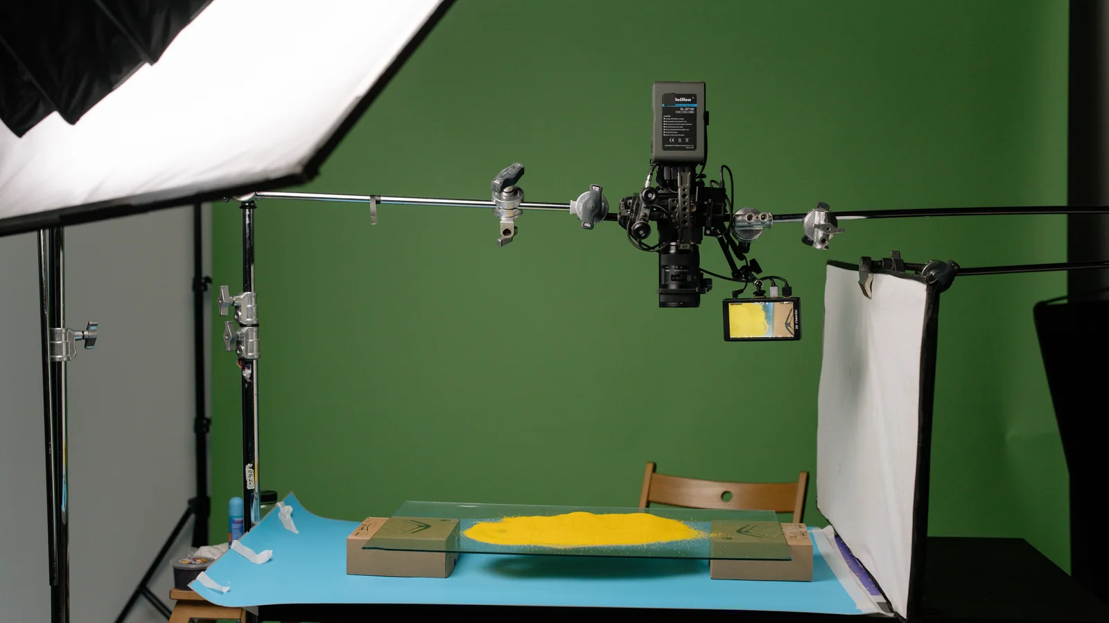 Overhead camera and studio lights above yellow sand on a glass tabletop