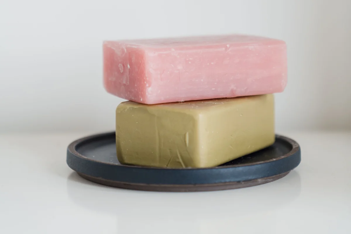 Pink and olive-green soap bars stacked on a dark dish against a white background
