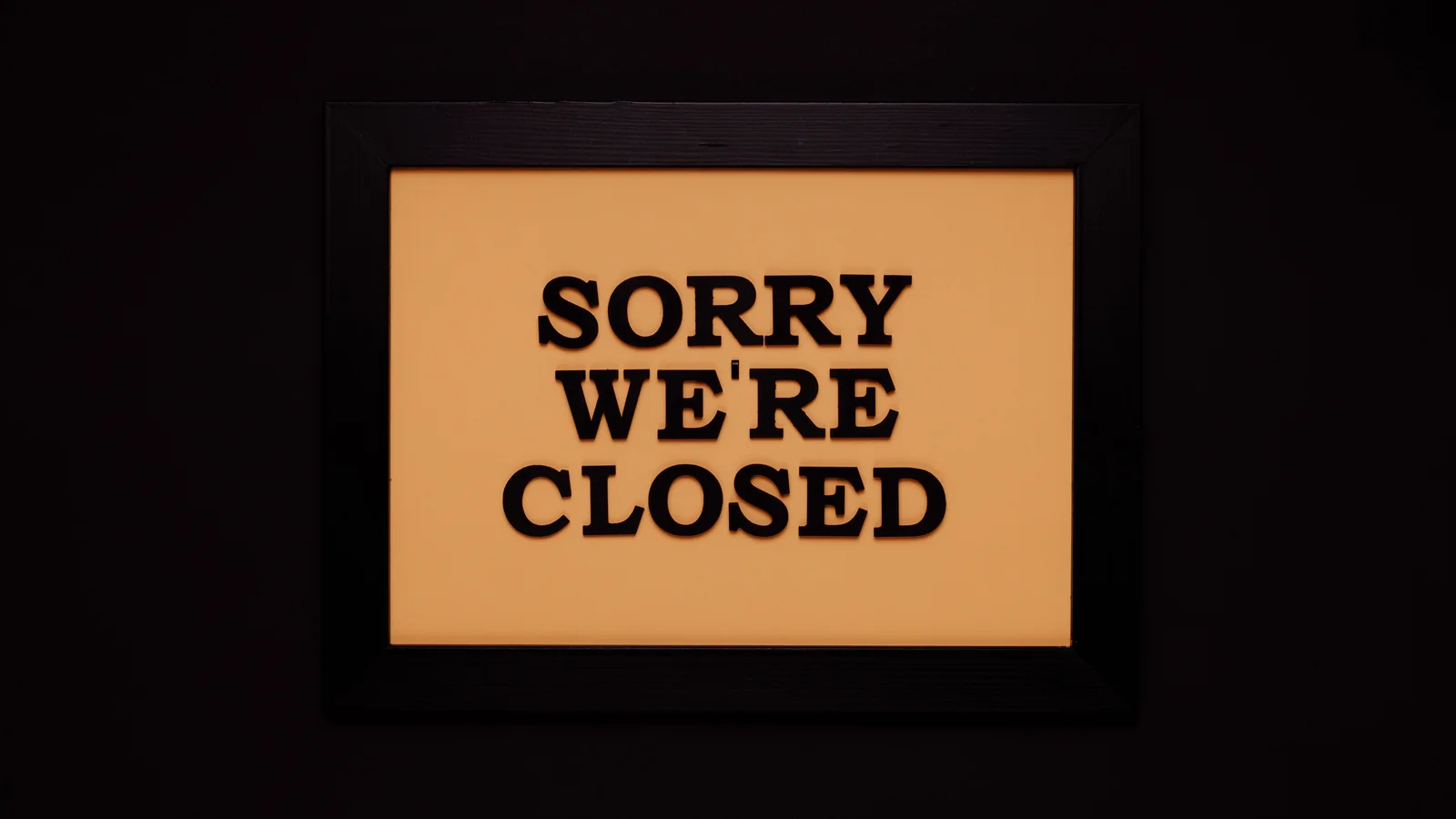 Black-framed 'Sorry We're Closed' sign against a dark background