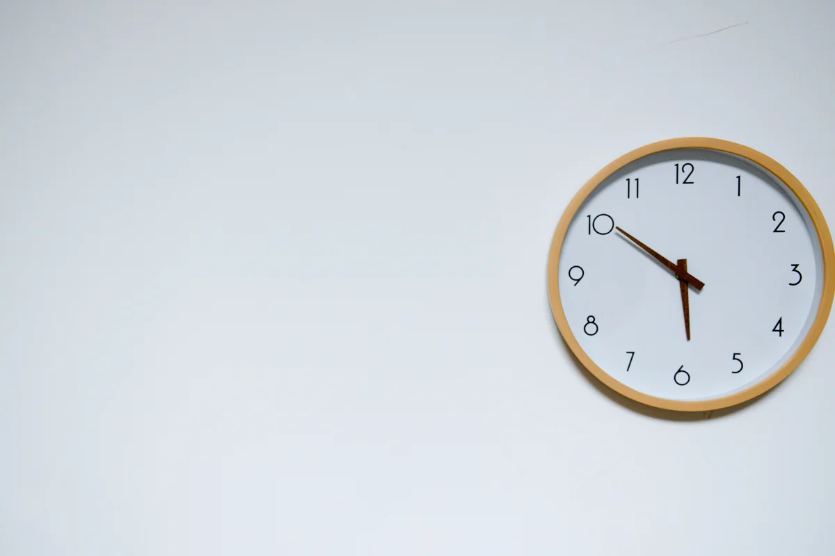 Simple wooden-framed analog wall clock on a plain white wall